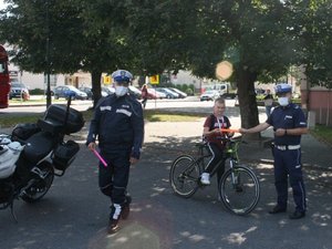 na fotografii dwaj policjanci ruchu drogowego, jeden wręcza odblask młodemu chłopcu na rowerze
