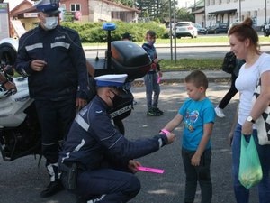 policjant ruchu drogowego przykucnął przed dzieckiem i wręcza mu odblaskową opaskę