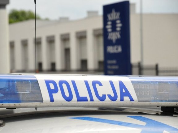 Na zdjęciu widoczna jest belka policyjnego radiowozu. Na dalszym planie widoczny jest budynek Komendy Powiatowej Policji w Jaśle.