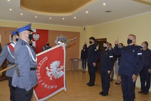 Komenda Miejska Policji w Przemyślu. Na pierwszym planie policjanci ze sztandarem jednostki. Ślubowanie trzech nowo przyjętych funkcjonariuszy, którzy składają rotę ślubowania w obecności komendanta i kierownictwa.