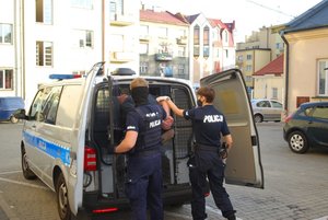 Na zdjęciu na dziedzińcu komendy do stojącego radiowozu volkswagen bus umundurowani policjanci wprowadzają podejrzanego celem przewiezienia do Sądy Rejonowego w Rzeszowie.