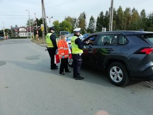 Policjant wręcza broszurę informacyjną kierującemu samochodem osobowym. Obok niego stoją: przedstawicielka PKP PLK S.A. oraz funkcjonariusz SOK.