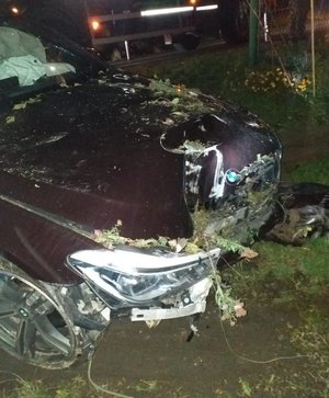 Na zdjęciu widać przód uszkodzonego pojazdu marki BMW. W tle elementy ogrodzenia.