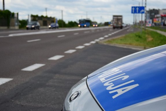 Maska policyjnego radiowozu. W tle rozmazany obraz jezdni i jadących samochodów.