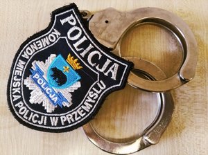 Zdjęcie kolorowe- przedstawia -na kajdankach położony emblemat Policji miejskiej w Przemyślu . W górnej części emblematu napis POLICJA , na środku korona w kolorze żółtym oraz herb miasta Przemyśl tz &quot;niedźwiedź&quot;