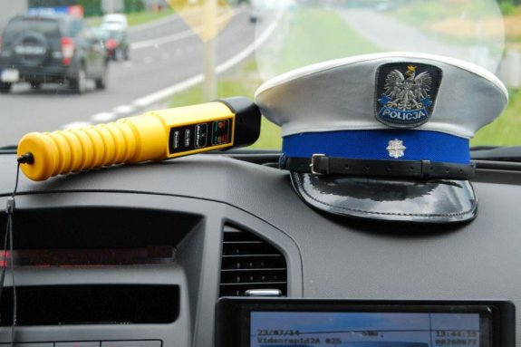 Wnętrze policyjnego radiowozu, w którym leży czapka i urządzenie do sprawdzania trzeźwości