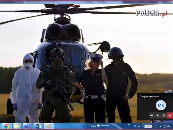 Obraz z ekranu na którym widać kadr z filmu ukazujący stojących przed helikopterem funkcjonariuszy policji.