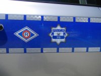 Zdjęcie kolorowe przedstawia bok radiowozy na niebieskim pasie widać naszywkę wydziału ruchu drogowego w kształcie rombu w środku litera R, a obok gwiazda policyjna.