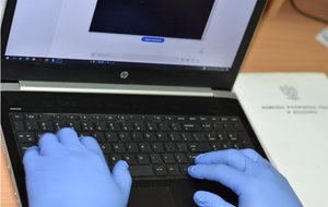 Na zdjęciu widać komputer i ręce policjanta na klawiaturze