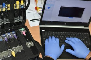 Na zdjęciu widać komputer i ręce policjanta na klawiaturze i sprzęt, którym dysponują