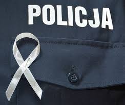 Zdjęcie przedstawia umundurowanego policjanta, który na piersi ma przypiętą białą wstążkę - symbol przeciwdziałania przemocy w rodzinie.