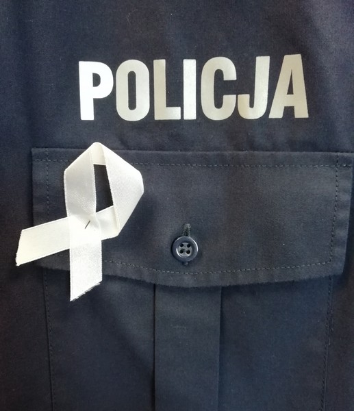 biała wstążka na granatowym tle policyjnego munduru. Powyżej biały napis policja
