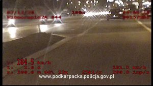 Stopklatka nagrania z policyjnego wideorejestratora. Pora nocna, samochód widoczny od tyłu. Czerwony napis wskazujący prędkość pojazdu 184,5 km/h.