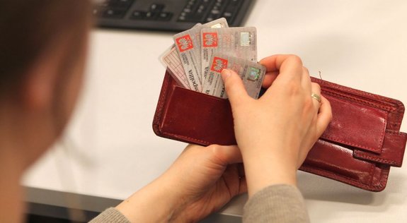 Na zdjęciu ręka trzymająca portfel w kolorze brązowym wkładająca dowody osobiste do środka