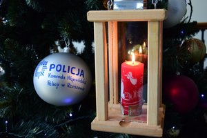 Zapalone betlejemskie światełko pokoju na tle choinki i bombki z napisem Komenda Wojewódzka Policji w Rzeszowie