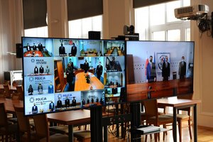 Na zdjęciu monitor, na którym widać sylwetki wielu osób podczas wideokonferencji