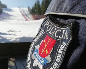 emblemat z napisem Komenda Powiatowa Policji w Ustrzykach Dolnych, w tle stok  narciarski