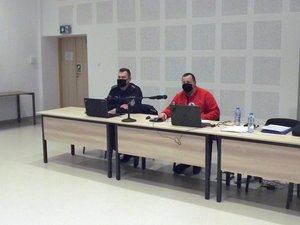 Uczestnicy szkolenia - policjanci i ratownicy STORAT na auli Oddziału Prewencji Policji w Rzeszowie. Policjant i ratownik siedzą przy stoliku.