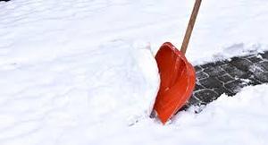 Zdjęcie kolorowe przedstawia chodnik zaprószony śniegiem oraz łopatę do odśnieżania. Łopata w kolorze czerwonym z drewnianym trzonkiem