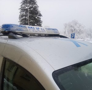 Na zdjęciu belka policyjna. W tle zaśnieżone drzewa i znak drogowy.