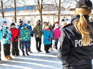 zdjęcie przedstawia policjantkę w umundurowaniu służbowym (od tyłu), a przed stojąca grupka dzieci