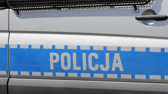 Zdjęcie kolorowe przedstawia bok pojazdy służbowego (Radiowozu) gabarytowego. Widoczne drzwi z napisem „POLICJA” oraz częściowo widoczna okratowana szyba.