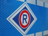 Zdjecie kolorowe przedstawia prawy bok radiowozu policyjnego oznakowanego na drzwiach pojazdy widoczny emblemat policyjnego wydziału ruchu drogowego w środku litera „R” tz. „ERKA”
