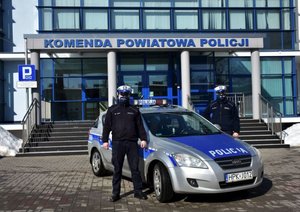Policjanci wydziału ruchu drogowego stoją obok radiowozu. W tle budynek Komendy Powiatowej Policji w Jarosławiu.