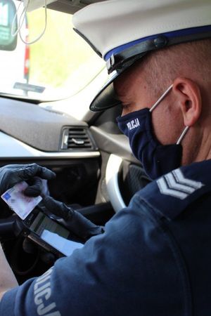 Na zdjęciu policjant, podczas kontroli drogowej, spisuje dane z dokumentu prawa jazdy