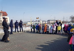 Policjanci, jeden z psem służbowym, stoją przed grupą dzieci.