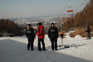 Zdjęcie kolorowe przedstawia stok narciarski w Przemyślu -widoczna panorama Przemyśla oraz stojace dwie policjantki tyłem a w środku stoi ratownik GOPR
