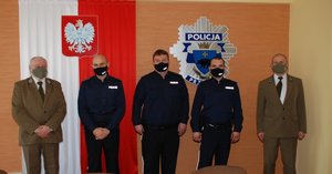 1. Zdjęcie przedstawia aulę w Komendzie Miejskiej Policji w Przemyślu .W tle widoczna jest ściana na środku której umieszczona jest flaga Polski z orłem wykonanym z metalu. Po prawej stronie zawieszone  jest logo policji tj. gwiazda policyjna.  Z lewej strony pod ścianą stoi Komendant Straży Leśnej Krzysztof Porczak, obok komendanta stoją trzej policjanci z Komisariatu Policji  w Dubiecku a z lewej strony widoczny Nadleśniczy Przemysław Włodek.