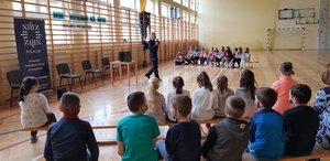 Sala gimnastyczna Szkoły Podstawowej w Wiśniowej, na pierwszym planie widać siedzące dzieci i nauczycieli, w tle policjanci.