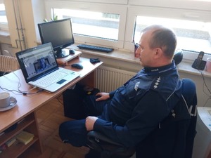 Policjant przed monitorem komputera podczas wideokonferencji z młodzieżą.