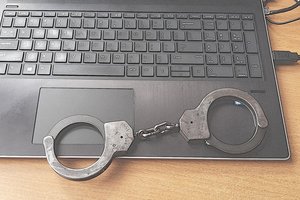 Fragment komputera osobistego - laptopa, na klawiaturze leżą stalowe kajdanki policyjne koloru czarnego.
