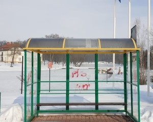 Zdjęcie zrobione w porze zimowej dookoła widoczny jest śnieg.Fotografia przedstawia wiatę autobusową w miejscowości Medyka. Wiata jest oszklona  jej łączenia są metalowe pomalowane na kolor zielony. Dach przystanku jest pokryty plastikową szybą której zakończenia są pomalowane na kolor żółty. W tle fotografii po lewej stronie widoczny jest budynek szkoły. Za przystankiem umieszczona jest czerwona tablica  z nieczytelną treścią w kolorze białym. Po prawej stronie stoją trzy słupy latarni.