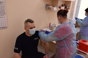 Komendant Powiatowy policji w Jarosławiu w trakcie szczepienia przeciwko Covid-19. Szczepionkę podaje pielęgniarka.
