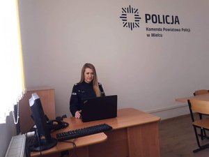 na fotografii policjantka w umundurowaniu służbowym, siedząca za biurkiem na którym leży komputer