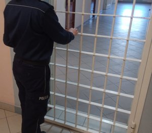 Na zdjęciu policjant, który zamyka drzwi pomieszczenia dla osób zatrzymanych.