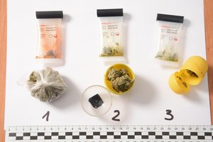Na zdjęciu worek foliowy i dwa plastikowe pojemniki z zawartością suszu roślinnego, powyżej trzy testery narkotykowe, poniżej skalówka.