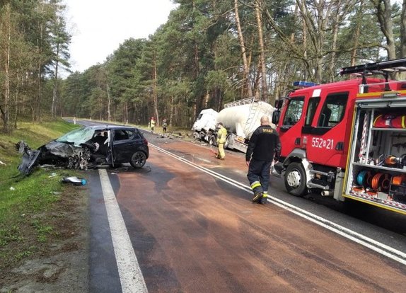 Miejsce wypadku drogowego. Na pierwszym planie uszkodzony pojazd opel corsa, na drugim planie ciężarowy Daf w rowie.