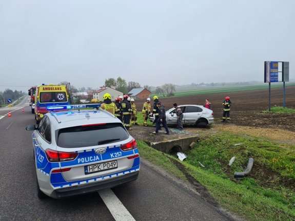 Zdjecie kolorowe przedstawia drogę krajową K77 w miejscowości Zadąbrowie (miejsce zdarzenia drogowego. ) Po prawej stronie zdjęcia widoczny radiowóz policyjny oznakowany, przed radiowozem widoczny jest Ambulans w kolorze żółtym. Po prawej stronie widoczne pole orne na którym stoi samochód marki Seat koloru srebrnego, do okoła pojazdu widoczni są Strażacy.W oddali widoczne zabudowania mieszkalne.