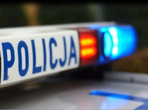 Zdjęcie kolorowe przedstawia belkę świetlną pojazdu uprzywilejowanego policyjnego. Belka posiada napis „POLICJA” który jest napisany niebieskimi literami na białym tle, obok napisu widoczne światło czerwone a obok niebieskie.