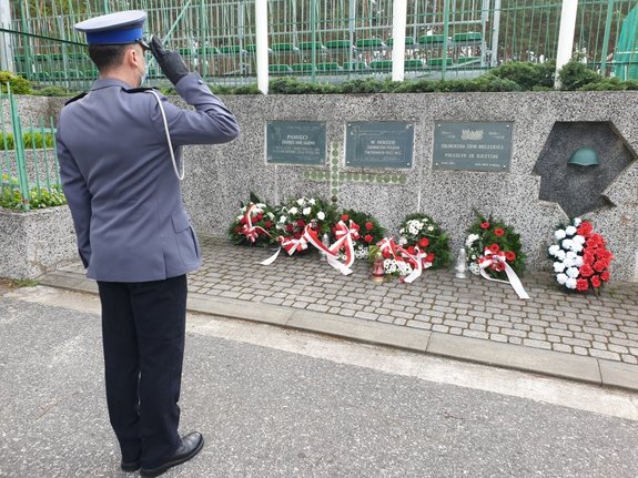 podinsp. Grzegorz Bajda podczas składania kwiatów pod tablicami upamiętniającymi żołnierzy poległych w czasie II Wojny Światowej, policjant stoi przed tablicami z kwiatami