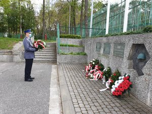 policjant stoi z kwiatami przed tablicami upamiętniającymi żołnierzy poległych w czasie II Wojny Światowej