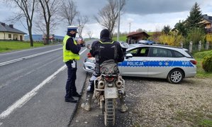 na poboczu drogi motocyklista na motocyklu, po lewej stronie policjant, z prawej strony oznakowany radiowóz