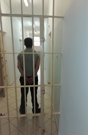 Zatrzymany 26 - latek stoi w pomieszczeniu dla osób zatrzymanych.