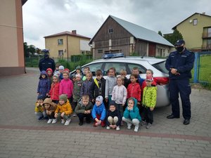 Policjanci oraz przedszkolaki stoją przy radiowozie