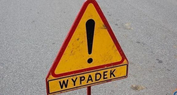Zdjęcie kolorowe przedstawia znak drogowy ostrzegawczy trójkąt koloru żółtego z czerwoną obwódką, w środku znaku jest umieszczony znak „Wykrzyknik” w czarnym kolorze pod znakiem umieszczona tabliczka na żółtym tle napis „WYPADEK” w kolorze czarnym