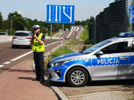 Policjant Wydziału Ruchu Drogowego kontroluje prędkość kierowców za pomocą ręcznego urządzenia pomiarowego przy drodze krajowej 94.